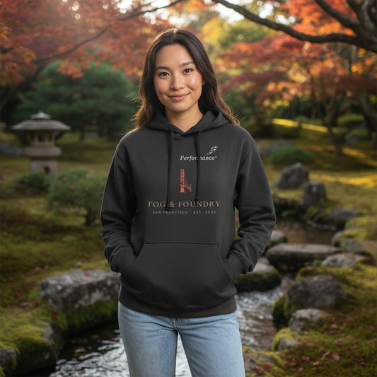 Woman wearing a black Fog & Foundry cotton fleece hoodie with a San Francisco bridge graphic in a park setting.