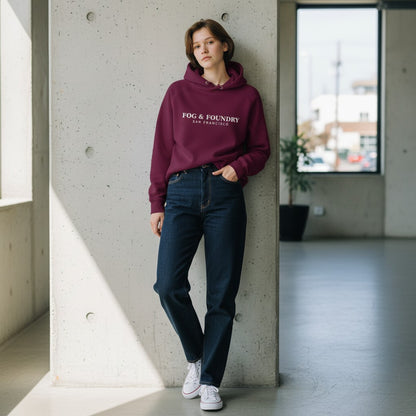 Model wearing a burgundy Fog & Foundry organic cotton raglan hoodie with white logo, paired with dark jeans.