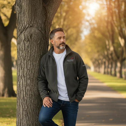 Man wearing a Fog & Foundry Columbia fleece jacket in dark grey, layered over a white t-shirt and jeans in a park.