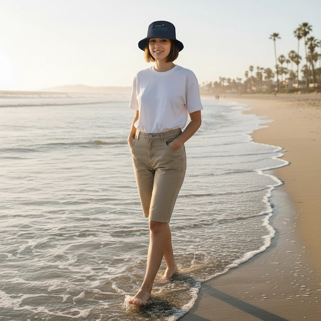 Woman wearing a Fog & Foundry cotton twill bucket hat while walking along the beach at sunset.