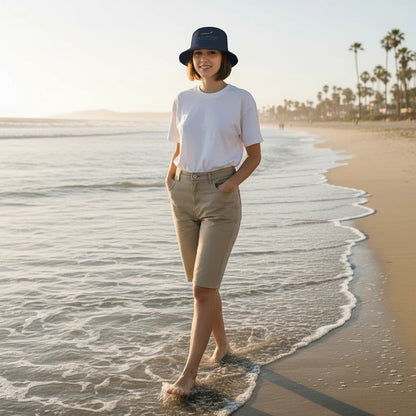 Woman wearing a Fog & Foundry cotton twill bucket hat while walking along the beach at sunset.