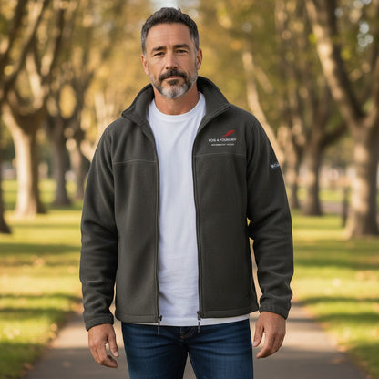 A man wearing a dark grey Fog & Foundry fleece jacket with a full-zip front, standing on a tree-lined path.