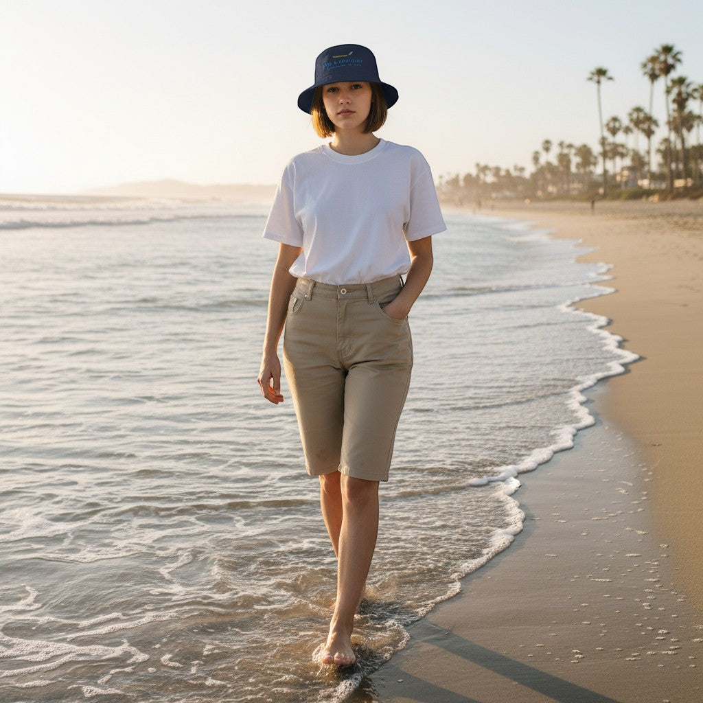 Woman wearing a Fog & Foundry gray cotton twill bucket hat walking along a sandy beach at sunset.