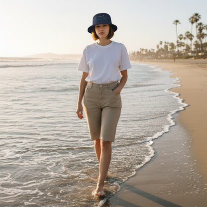 Woman wearing a Fog & Foundry gray cotton twill bucket hat walking along a sandy beach at sunset.