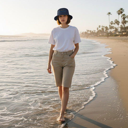 Woman wearing a Fog & Foundry gray cotton twill bucket hat walking along a sandy beach at sunset.