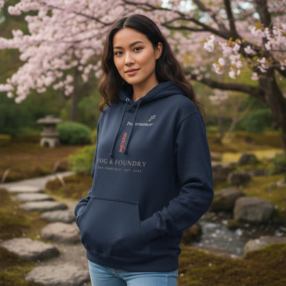 A woman wearing a navy blue Fog & Foundry cotton fleece hoodie with a front pouch pocket in a park with cherry blossoms.