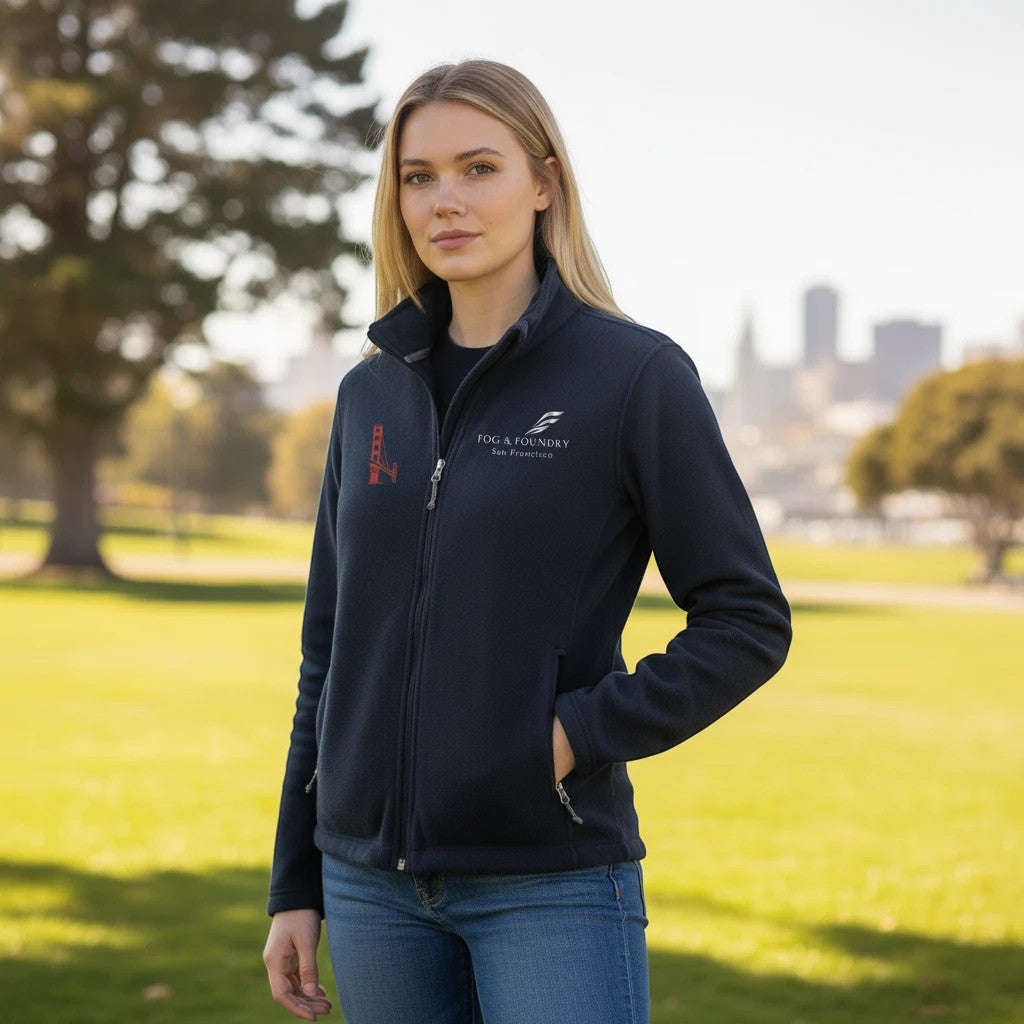 A woman wearing a navy blue Fog & Foundry full-zip fleece jacket with a stand-up collar in an outdoor park setting.