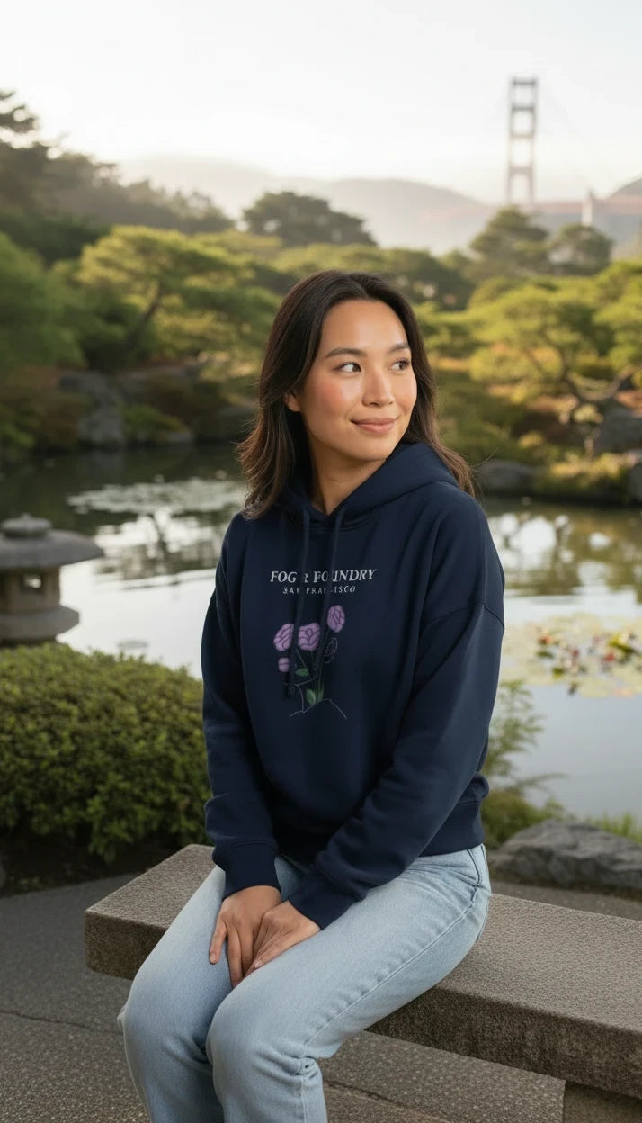 Woman wearing a navy Fog & Foundry organic cotton mid-length hoodie with a floral graphic in a park setting.