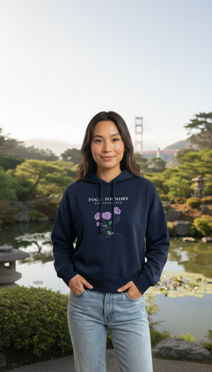 Woman wearing a navy Fog & Foundry organic cotton mid-length hoodie with a floral graphic in a park setting.