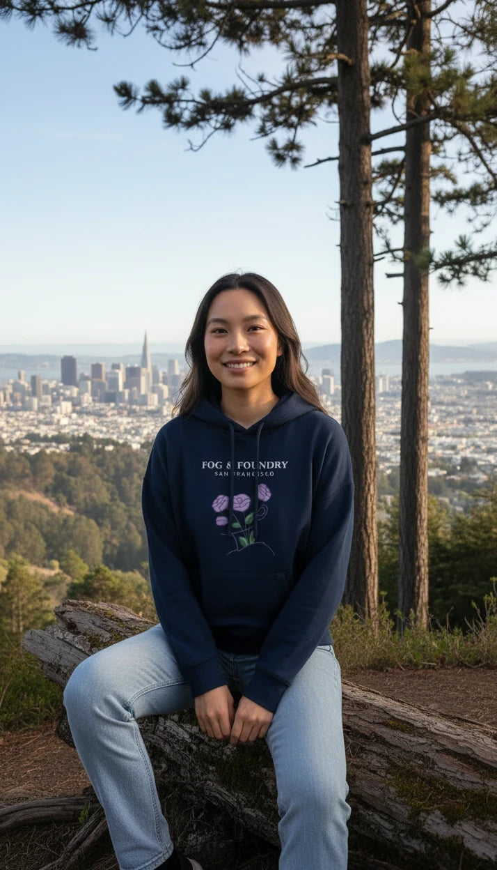 Woman wearing a navy Fog & Foundry organic cotton mid-length hoodie with a floral graphic, sitting on a log.