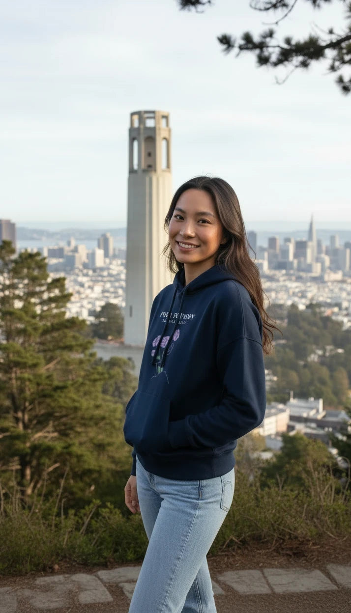 Woman wearing a navy Fog & Foundry organic cotton mid-length hoodie with a floral graphic in front of Coit Tower.