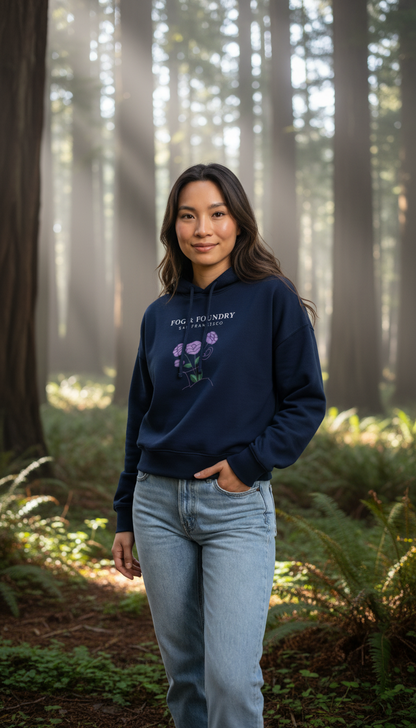 Woman wearing a Fog & Foundry navy organic cotton mid-length hoodie with floral graphic in a misty redwood forest.