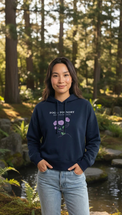 Woman wearing a navy Fog & Foundry organic cotton mid-length hoodie with a floral graphic in a forest setting.