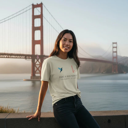 Woman wearing a Fog & Foundry organic cotton t-shirt with a hummingbird logo in front of the Golden Gate Bridge.