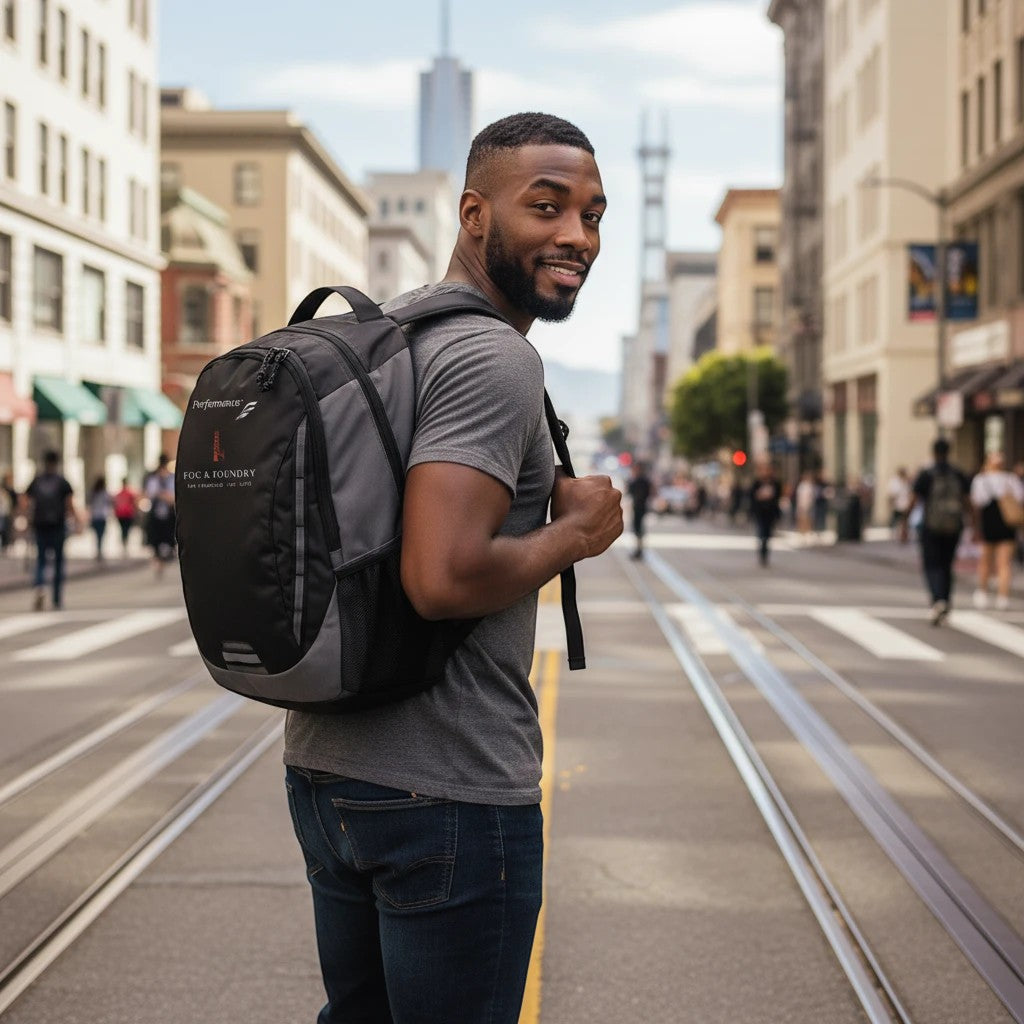 Man wearing a black Fog & Foundry Ridge backpack while walking on a city street with urban buildings in the background