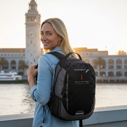 Woman wearing a black Fog & Foundry Ridge backpack by the San Francisco waterfront at sunset.