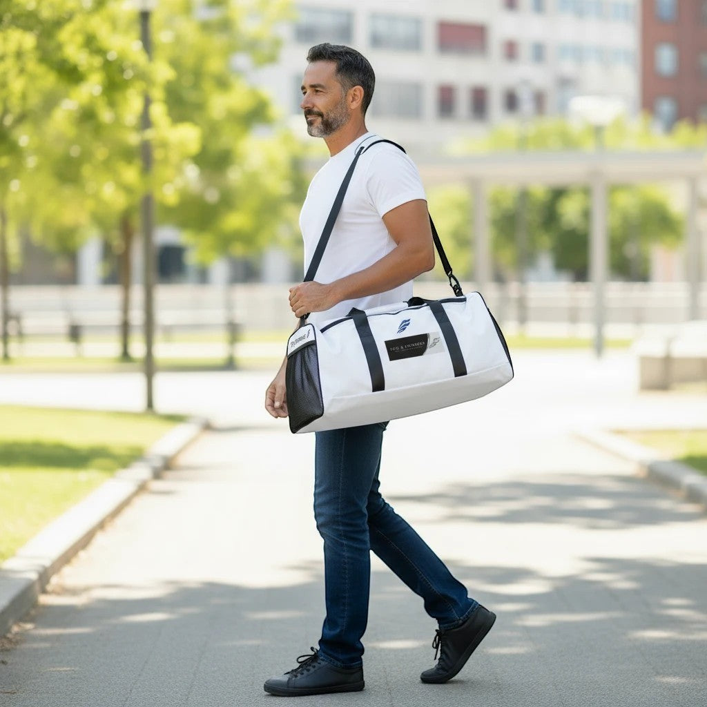 Man walking outdoors carrying a white and black Fog & Foundry polyester duffle bag with a padded shoulder strap.
