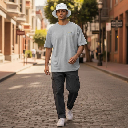 Man wearing a Fog & Foundry white cotton twill bucket hat and gray t-shirt walking on a city street.