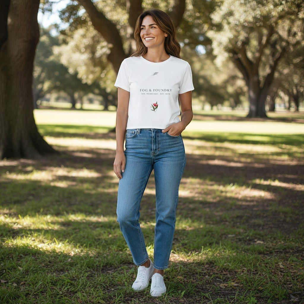 Woman wearing a white Fog & Foundry crop tee with a floral graphic and logo, styled with blue jeans in a park.
