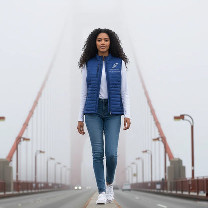 A woman wearing a blue Fog & Foundry quilted Marina Vest over a white long-sleeve shirt on a foggy bridge.