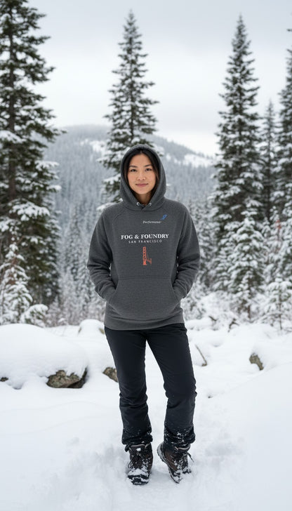 Woman wearing a charcoal grey Fog & Foundry organic cotton raglan hoodie in a snowy forest landscape.