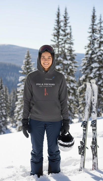 A woman wearing a charcoal grey Fog & Foundry organic cotton raglan hoodie in a snowy mountain setting with skis.