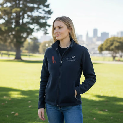 A woman wearing a navy blue Fog & Foundry full-zip fleece jacket with a stand-up collar in a park setting.