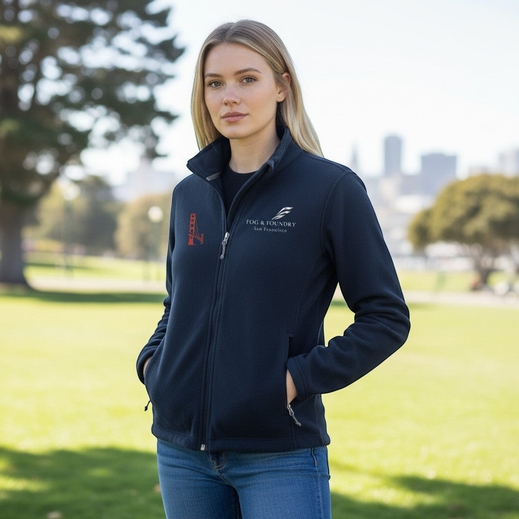 Woman wearing a navy blue Fog & Foundry full-zip fleece jacket with a stand-up collar and zippered pockets outdoors.