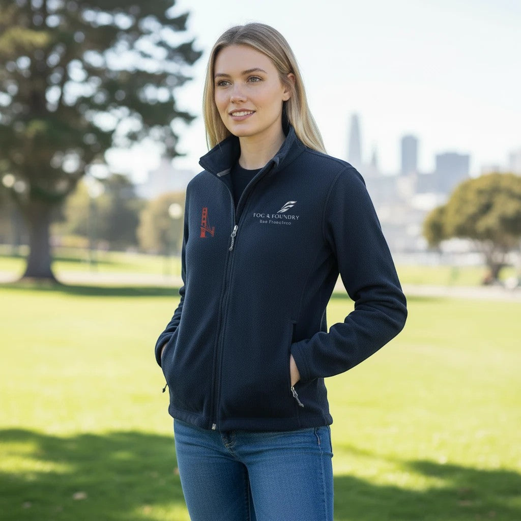 Woman wearing a navy blue Fog & Foundry full-zip fleece jacket with a stand-up collar and embroidered logo in a park.