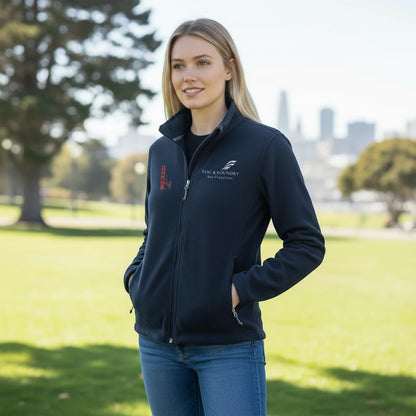 Woman wearing a navy blue Fog & Foundry full-zip fleece jacket with a stand-up collar and embroidered logo in a park.