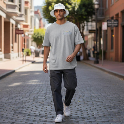 A man wearing a Fog & Foundry white cotton bucket hat and gray t-shirt walking down a city street.