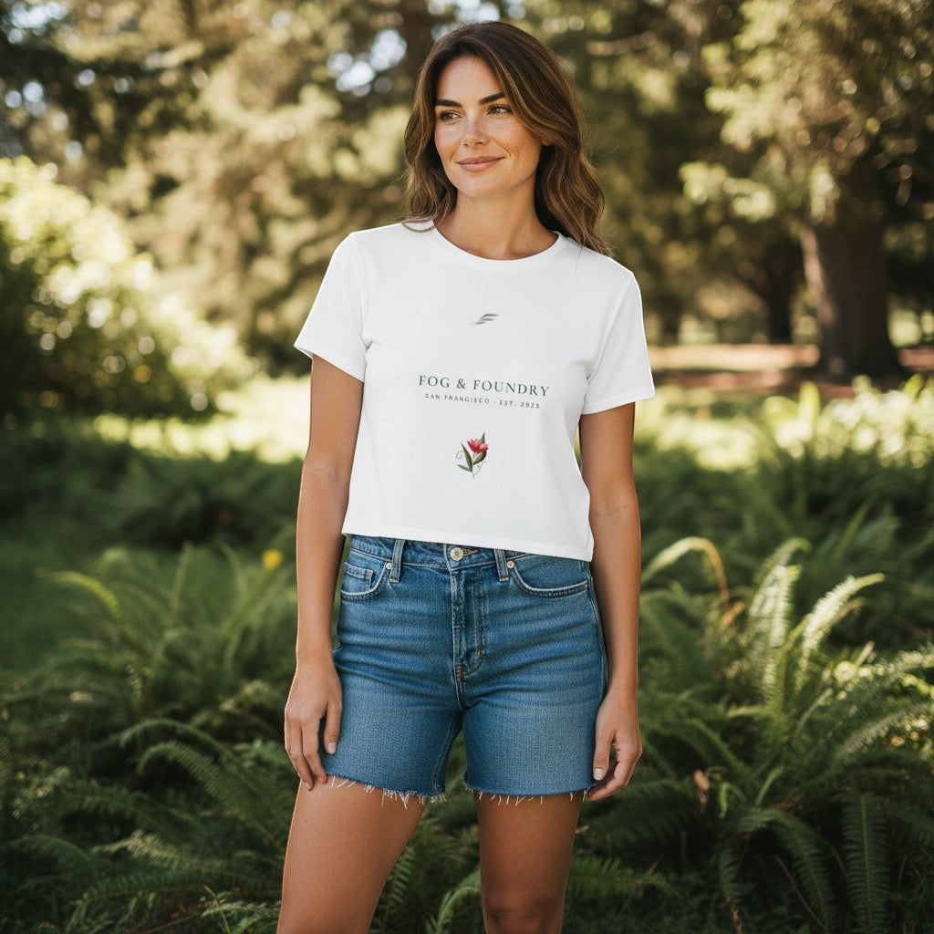 Woman wearing a white Fog & Foundry crop tee with a hand-drawn bloom graphic, styled with denim shorts in a park.