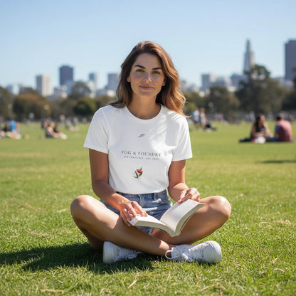Woman sitting on grass in a park wearing a white Fog & Foundry crop tee with a hand-drawn bloom and wordmark print.