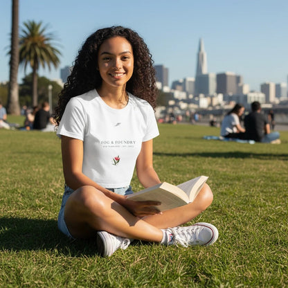 Woman wearing a white Fog & Foundry crop tee with a floral graphic, sitting on grass in a city park.